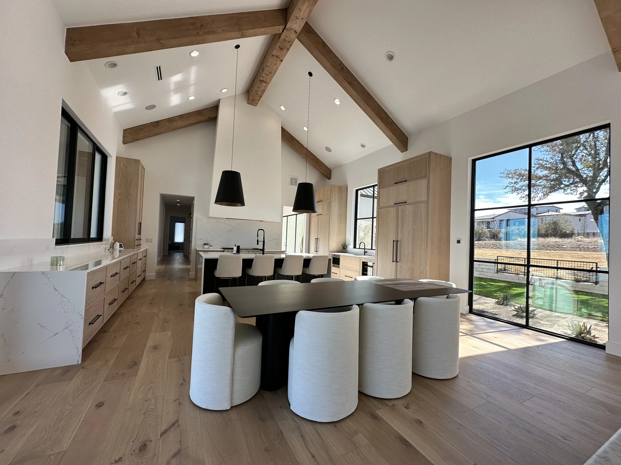 Vaulted kitchen and dining room with exposed beams, oak cabinetry, and pendant lights