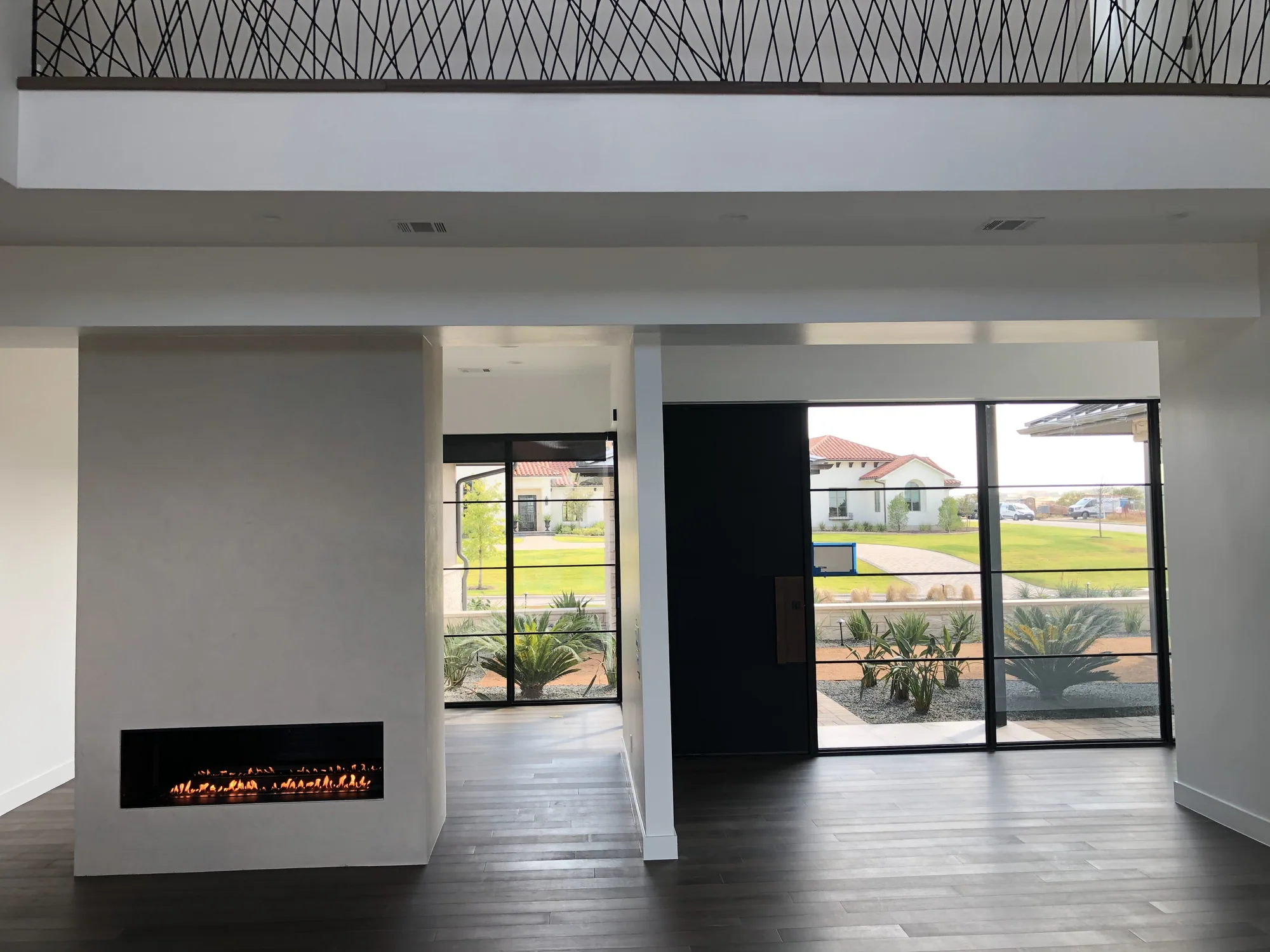 Double-sided fireplace dividing a light-filled living room beneath an open gallery