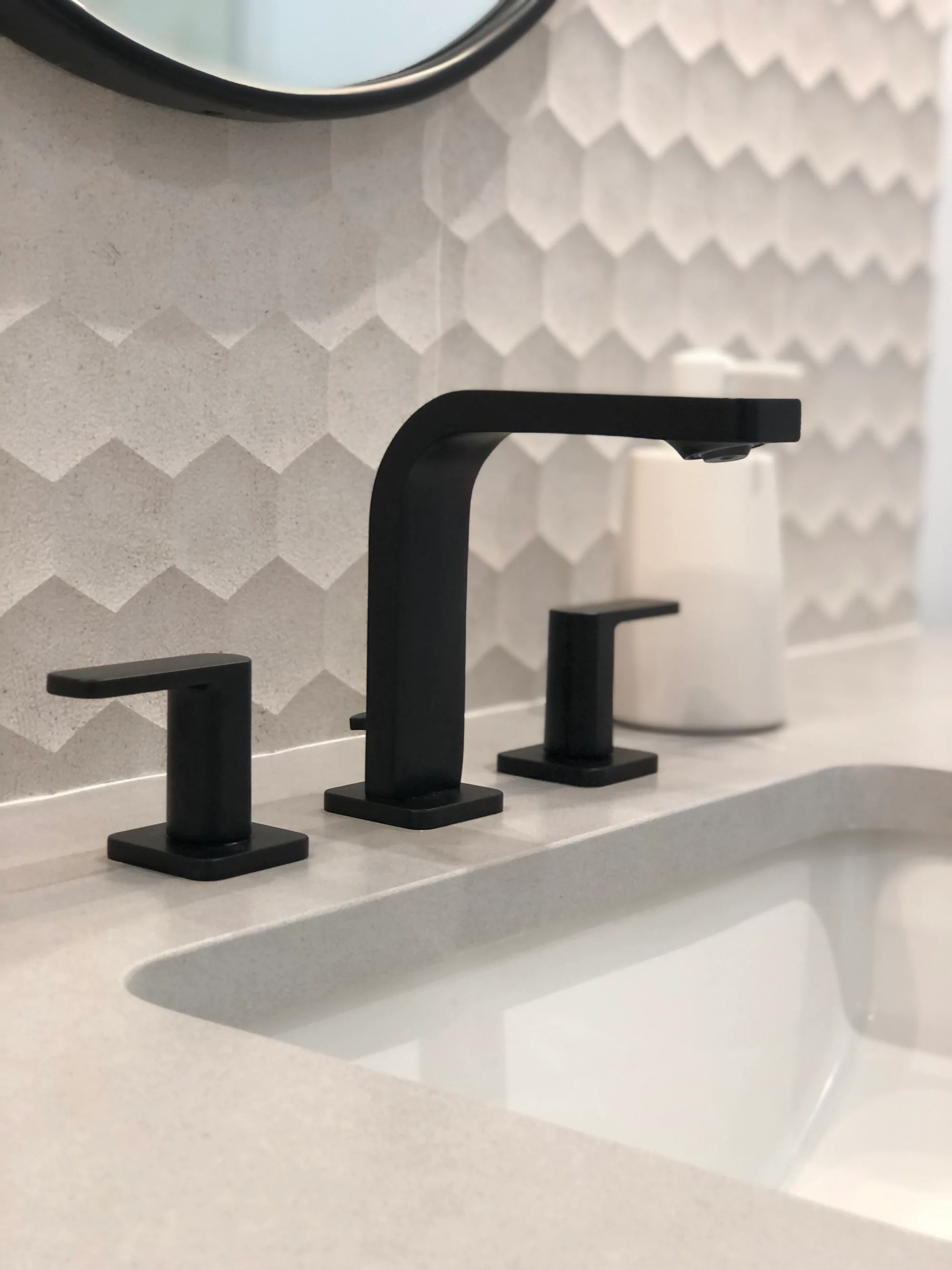 Matte black bathroom faucet against a dimensional white tile backsplash