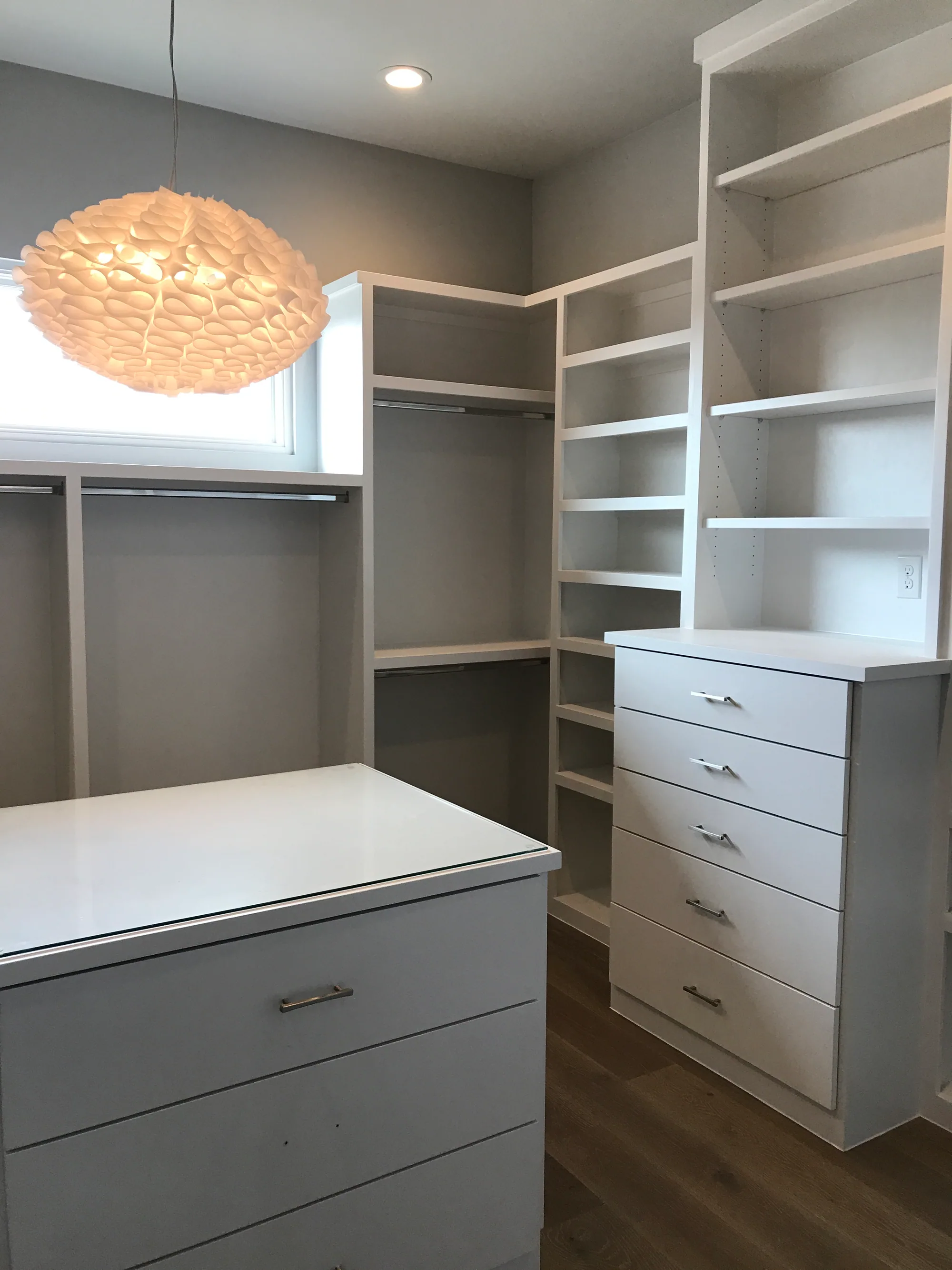 Custom dressing room with fitted drawers, open shelving, and a woven pendant