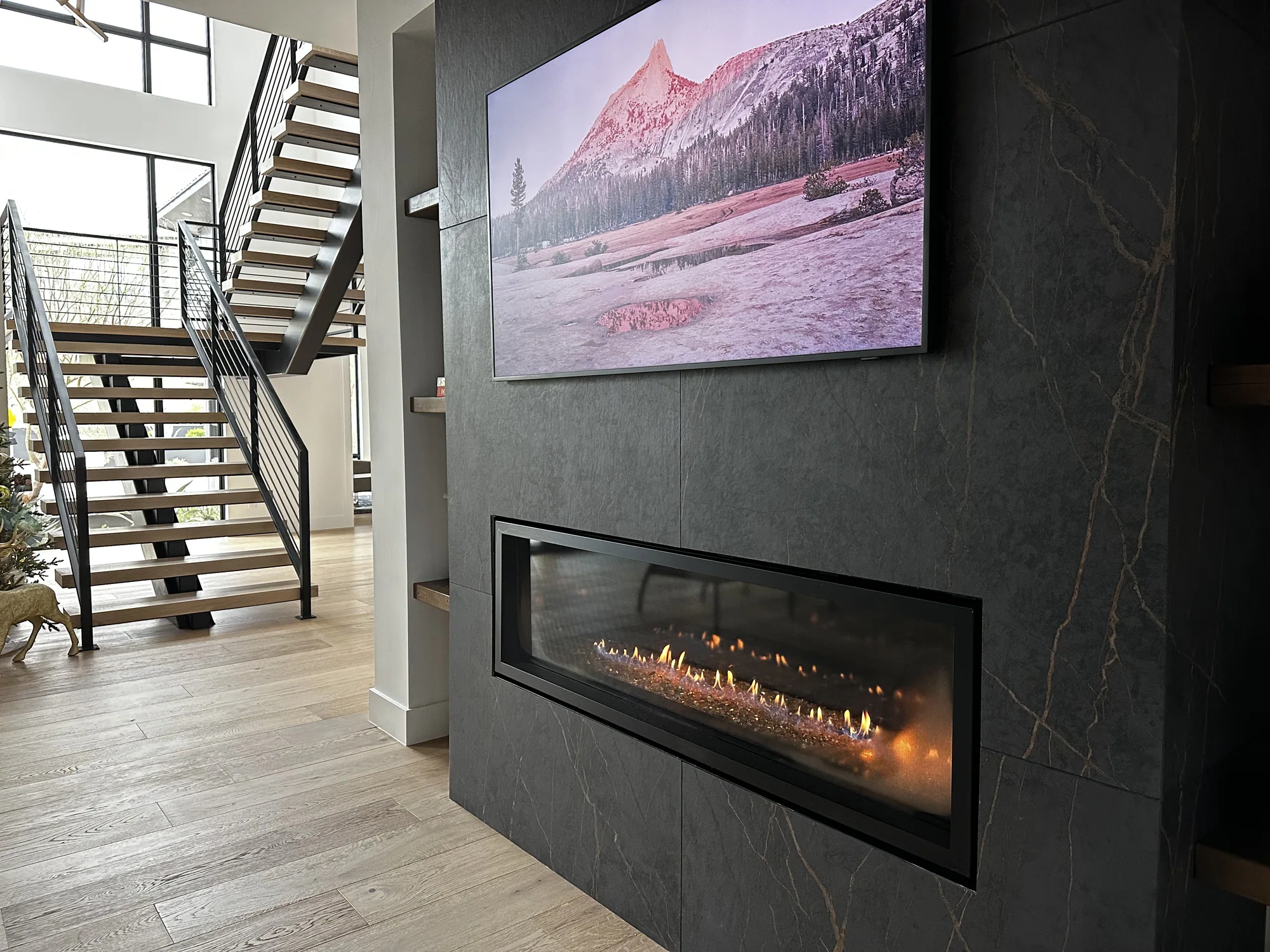 Dark stone fireplace beside an open staircase and full-height windows