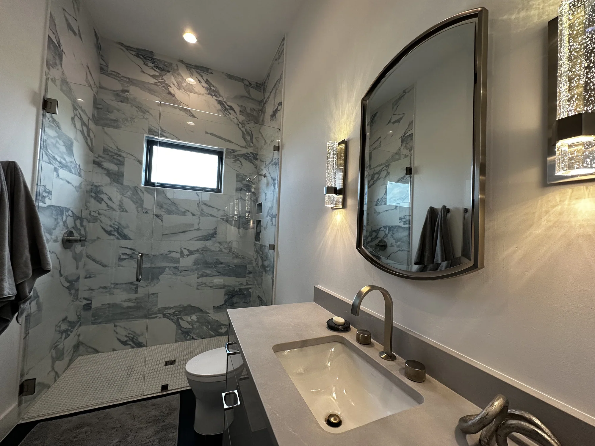 Marble shower and floating vanity with an oval mirror and wall sconces