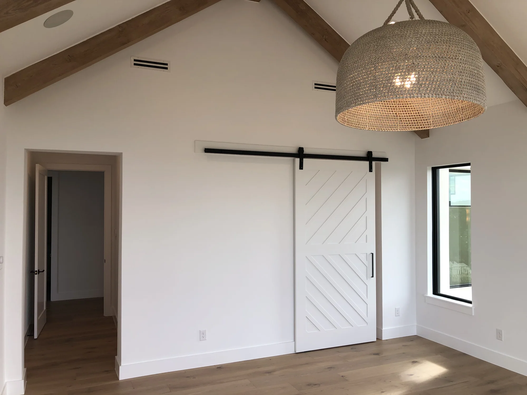 White chevron barn door beneath exposed wood beams and a woven pendant