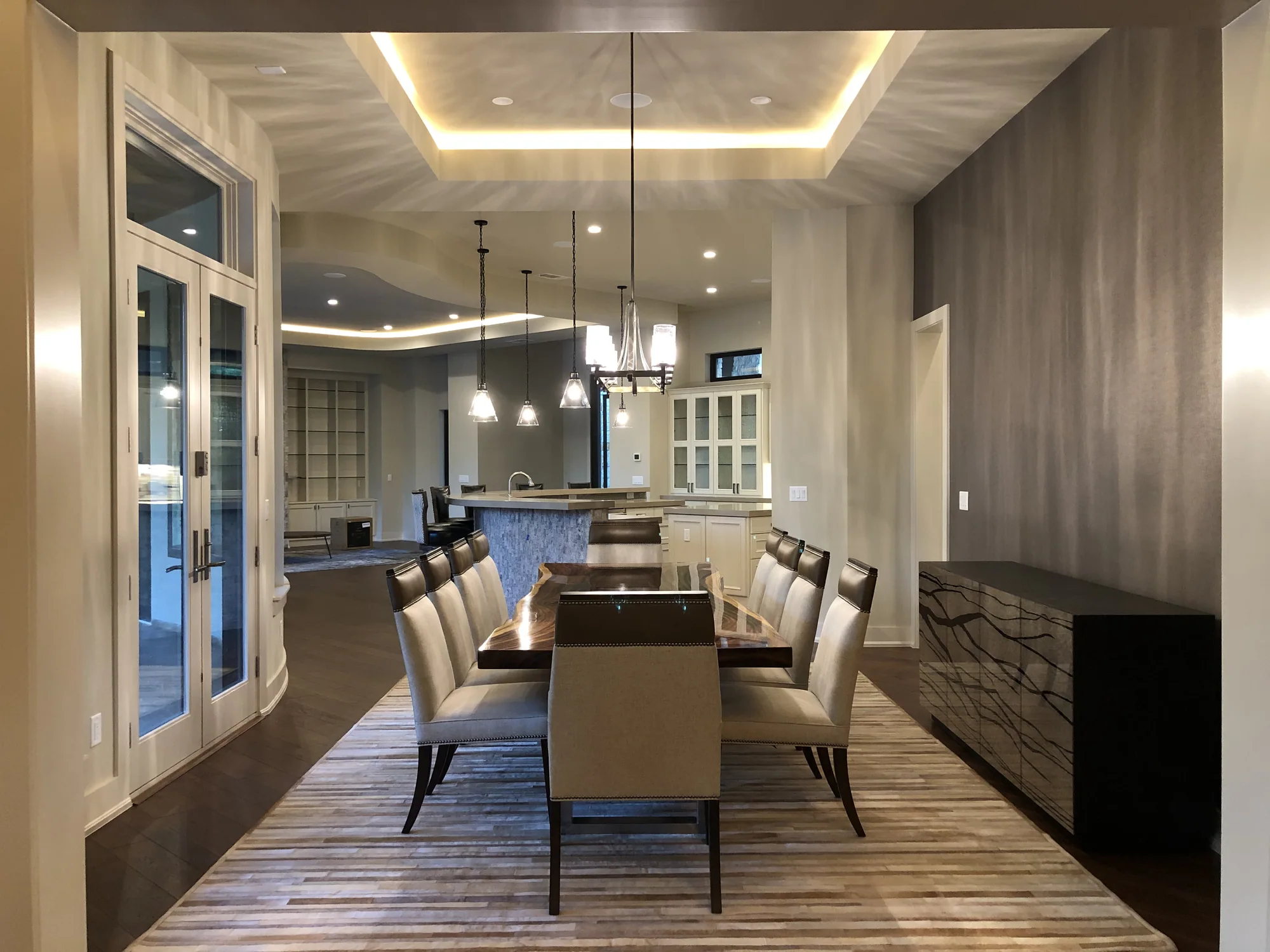 Long dining table beneath a tray ceiling with warm concealed lighting