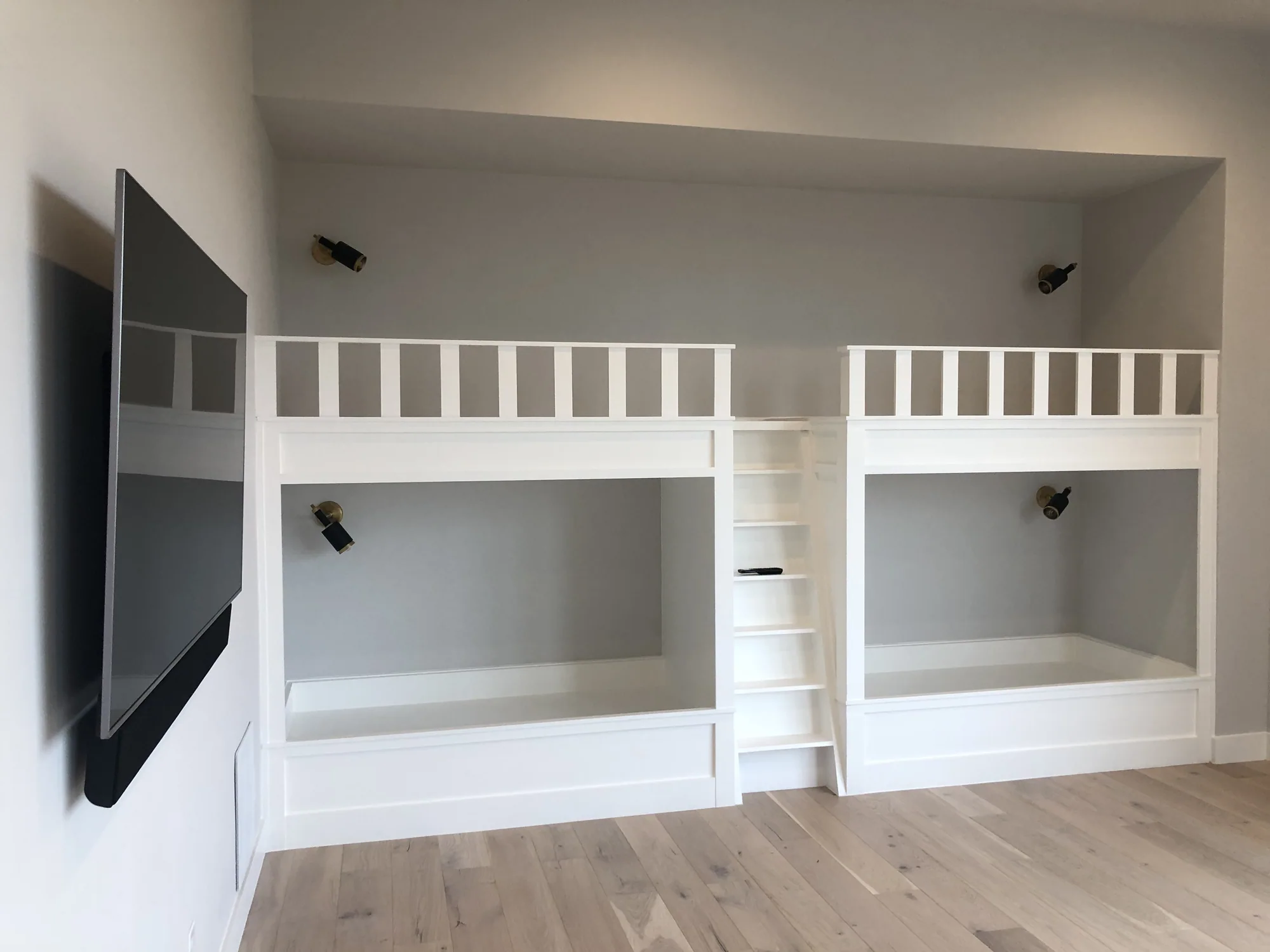 White built-in bunk beds with a central ladder and individual wall lights
