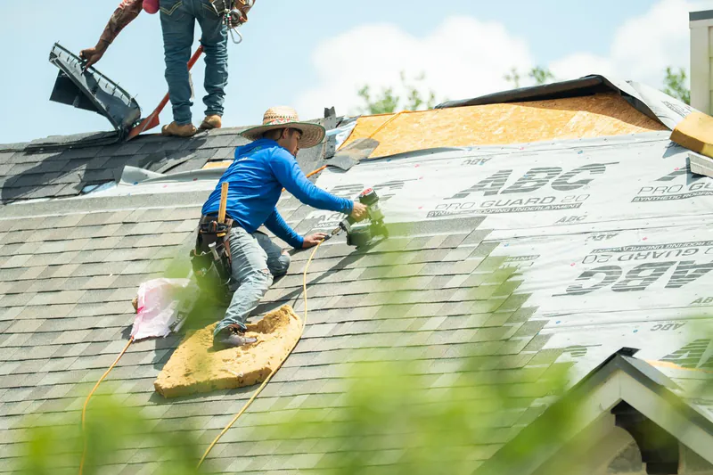 Roofer with safety harness nailing shingles